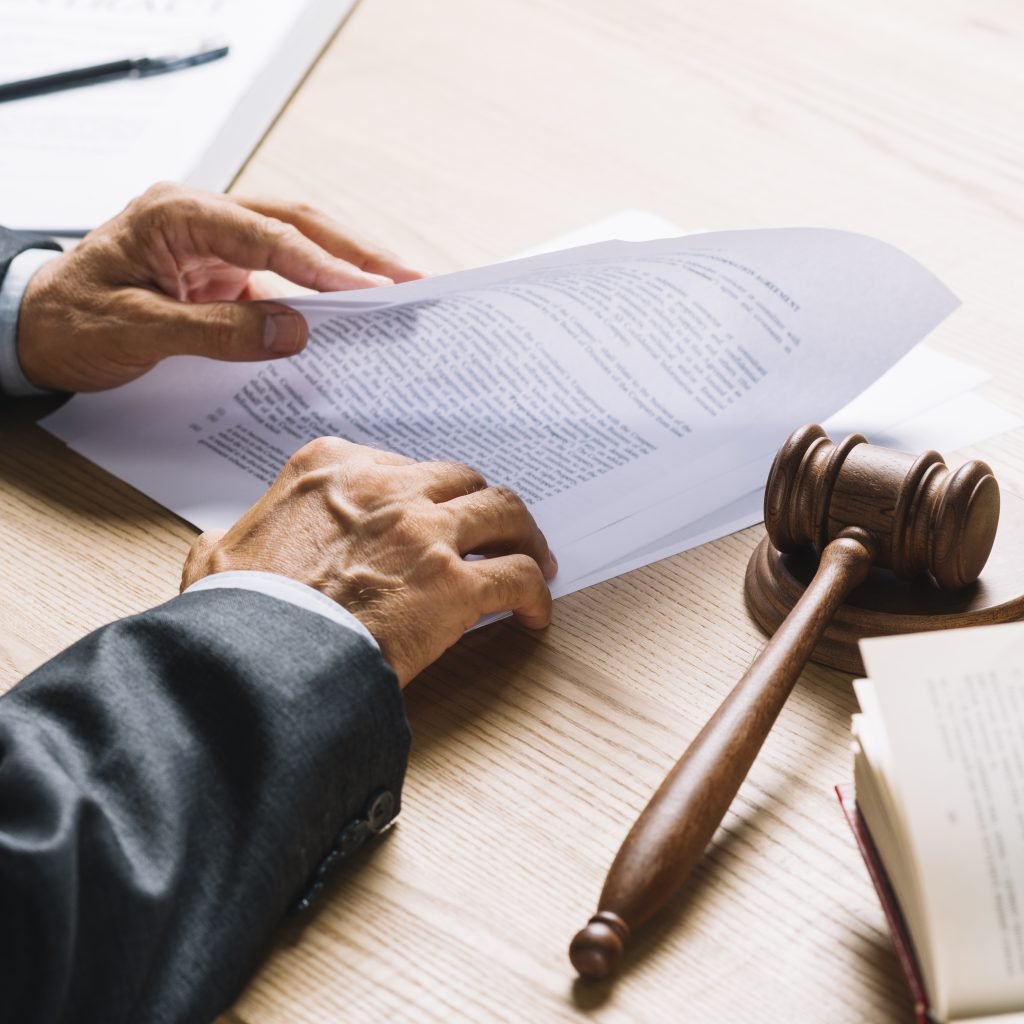 lawyer-s-hand-holding-document-with-gavel-mallet-wooden-desk